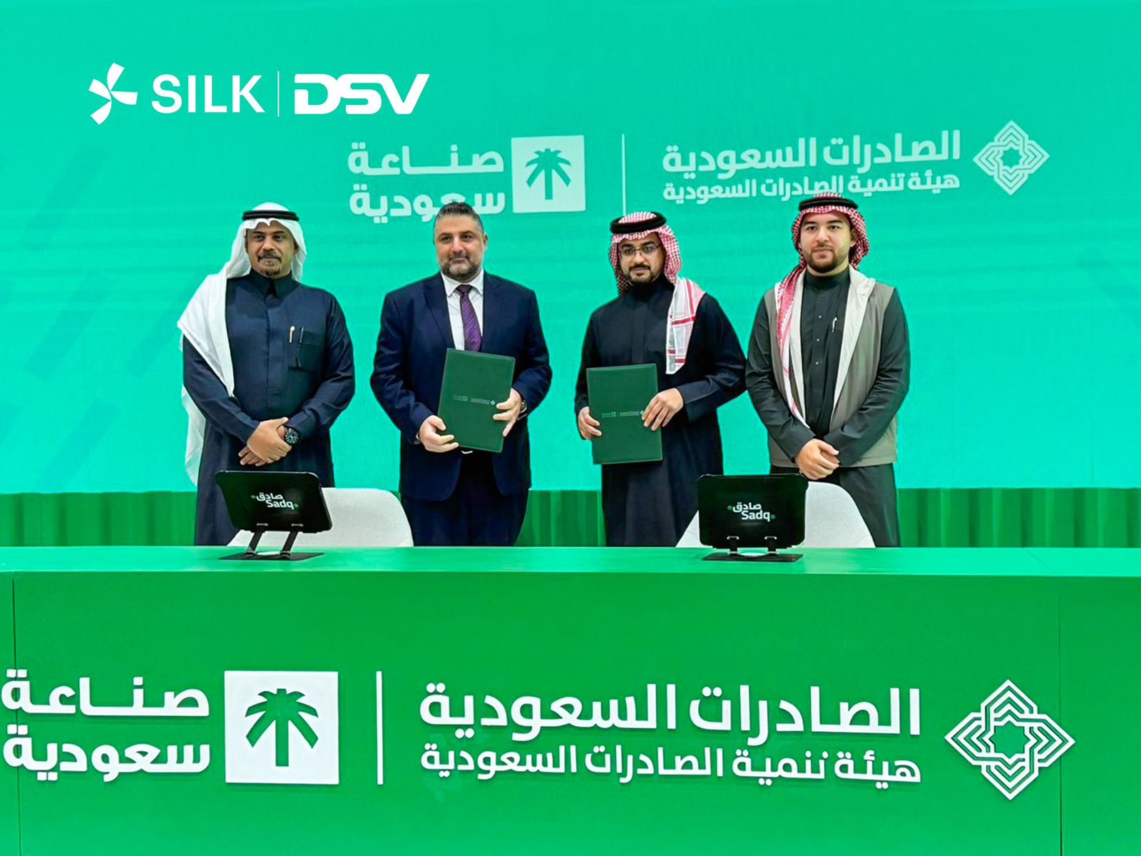 Four businessmen standing in front of Silk and DSV logos during a corporate signing event.