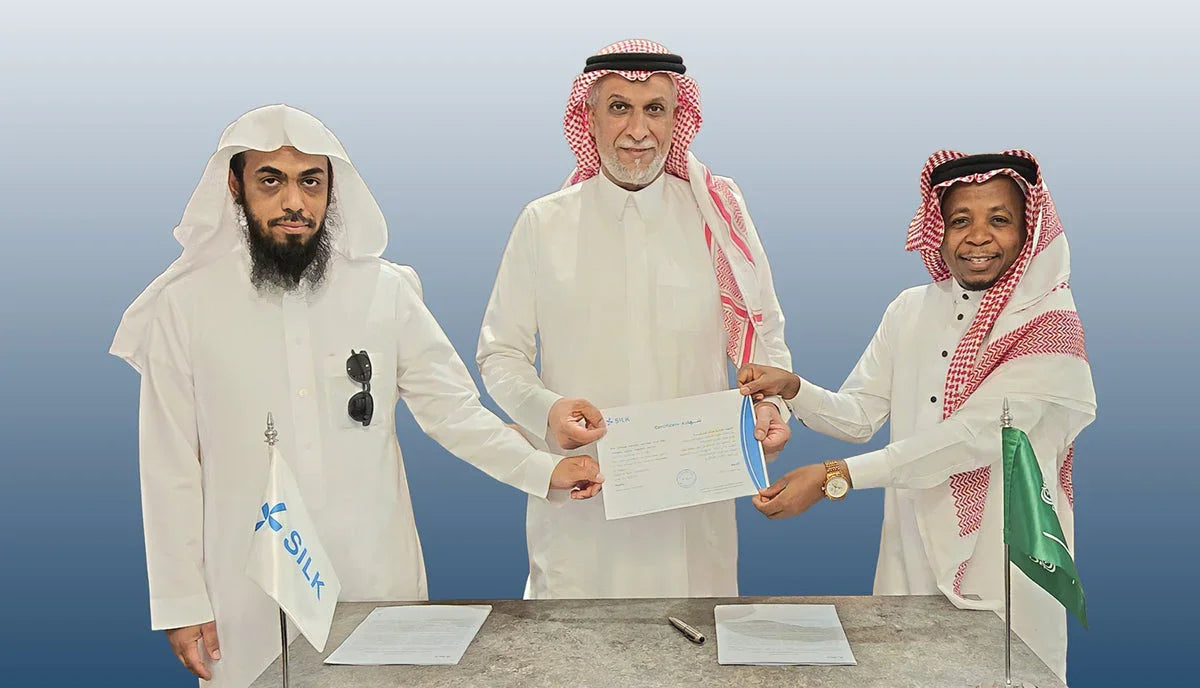 Three Saudi businessmen signing an agreement with a Silk branded flag on the table.