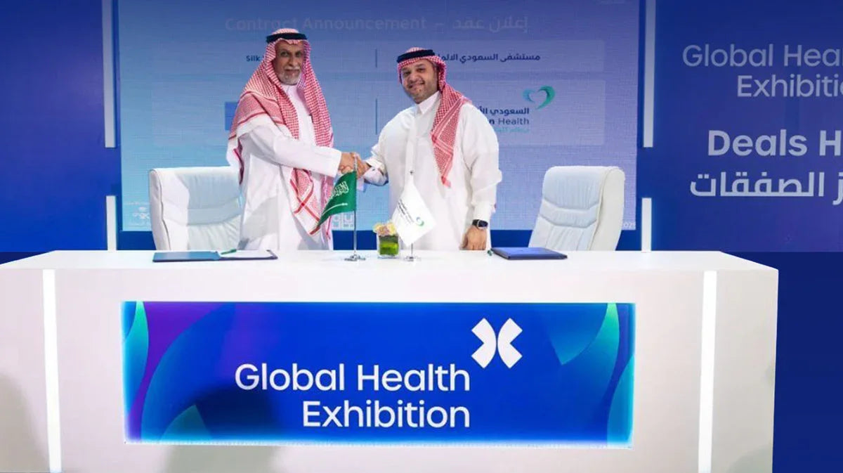 Two businessmen in traditional Saudi attire shaking hands at the Global Health Exhibition.