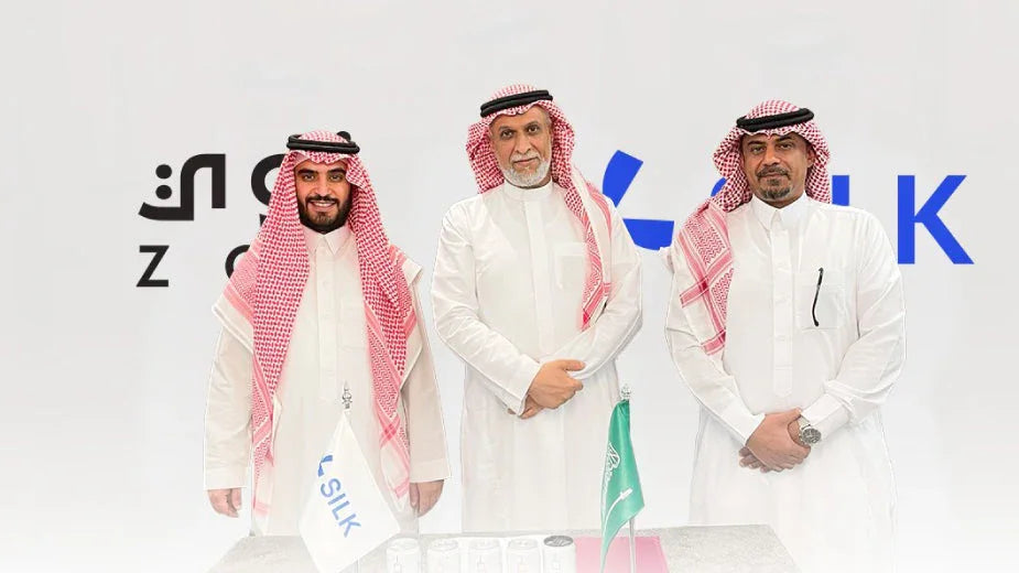 Three Saudi businessmen in traditional thobes and ghutras standing by a SILK flag.
