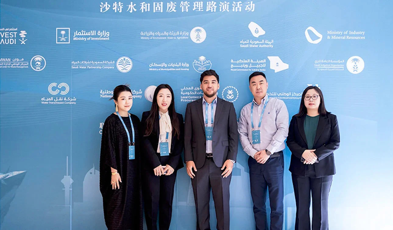 Five professionals standing in front of a corporate backdrop with government logos.